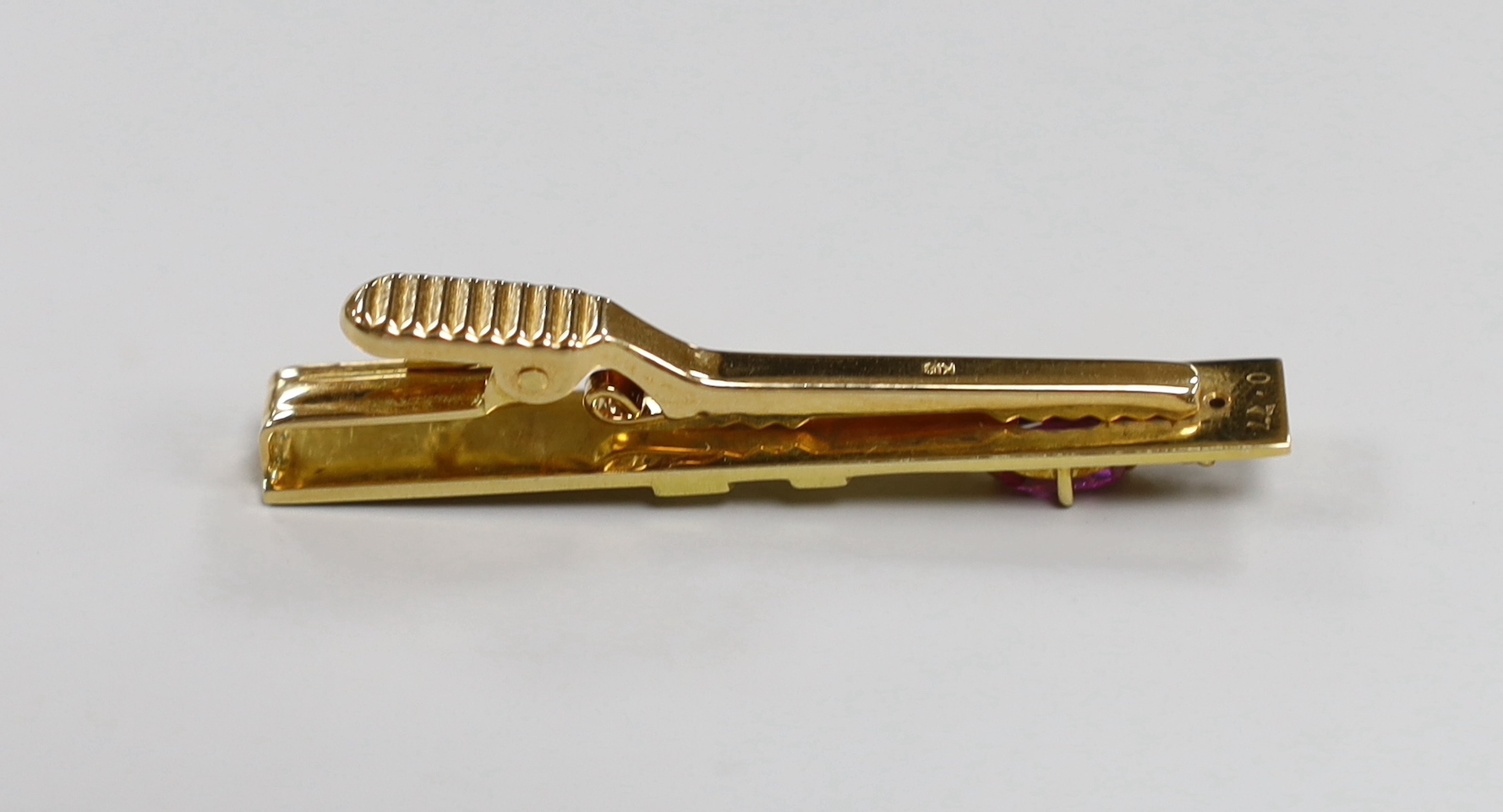 A modern 18k, ruby and diamond set three stone tie clip, 47mm, gross weight 7.7 grams.